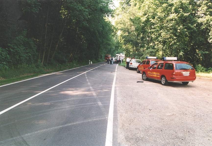 Straßenszene mit Einsatzfahrzeugen der Feuerwehr und Polizei, die am Straßenrand geparkt sind, während Einsatzkräfte in der Ferne auf der Straße arbeiten.