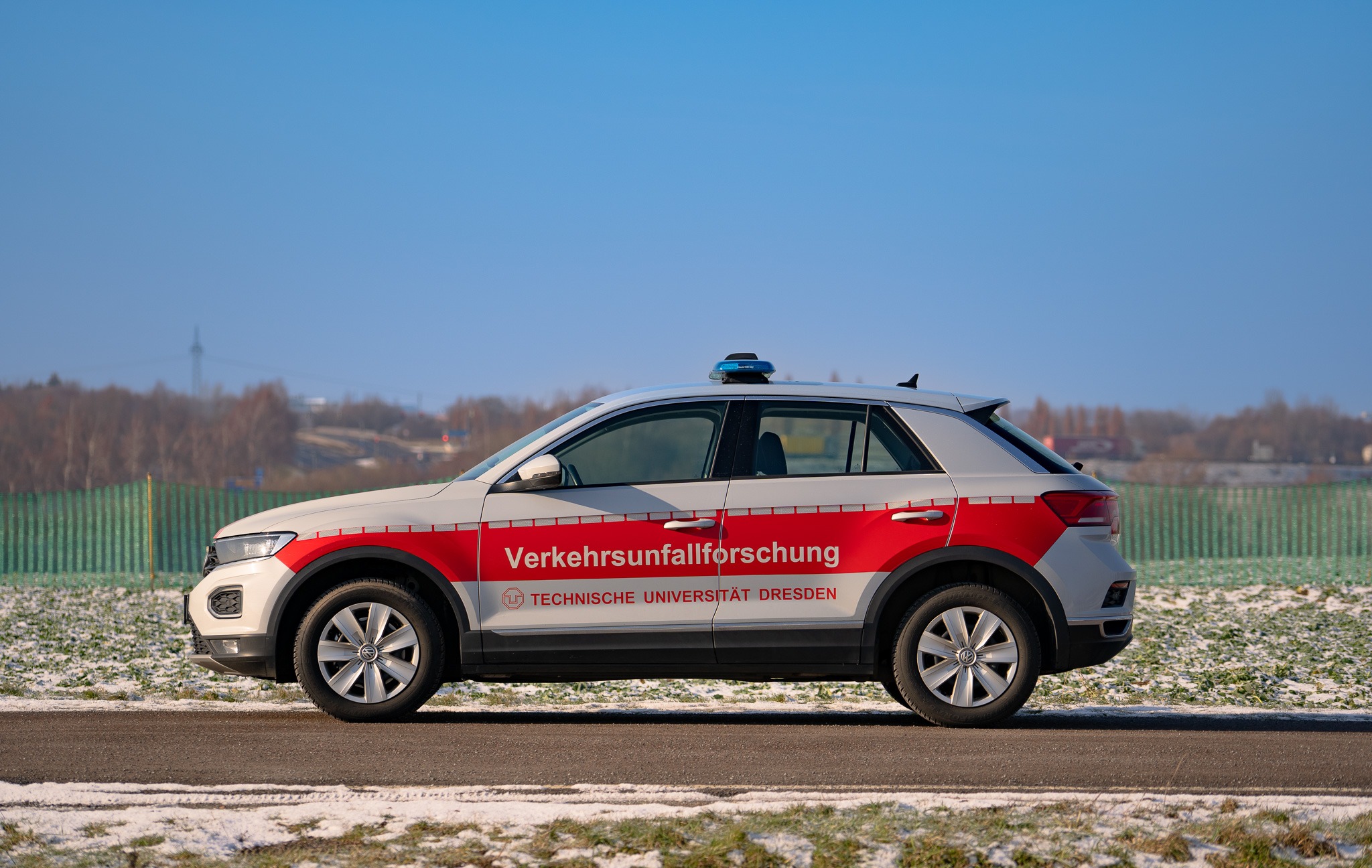 Traffic accident research vehicle from the Technical University of Dresden, pictured from the side, on a wintry road with light snowfall in the background.