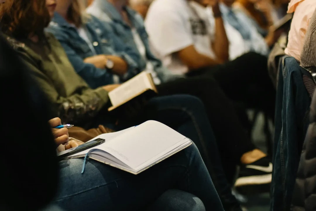 Seated listeners at an event with notebooks